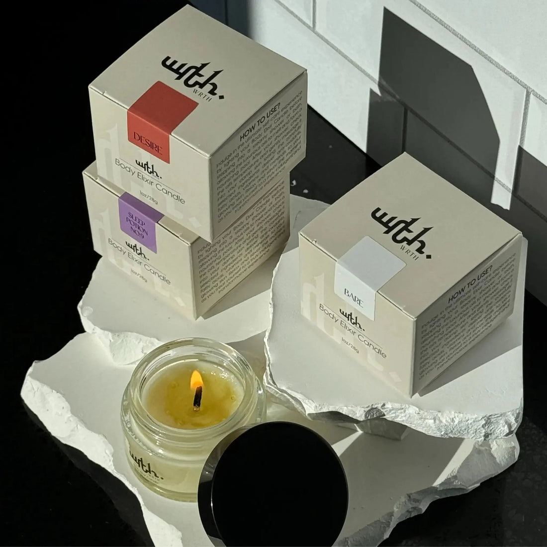 WRTH body elixir candles in Desire, Sleep Potion No9, and Bare scents displayed on white stone platters with one candle lit