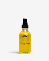 Yellow bottle of 'Cherry Musk' body oil with a black cap on a white background