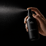 Hand holding a black 'Vanilla Musk' spray bottle against a dark background
