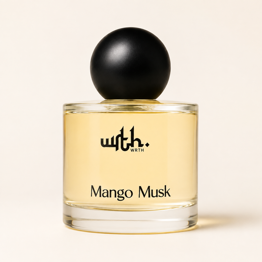 A bottle of with. WORTH Mango Musk fragrance, featuring a clear glass bottle filled with light golden-yellow liquid and topped with a matte black spherical cap, set against a warm off-white background.