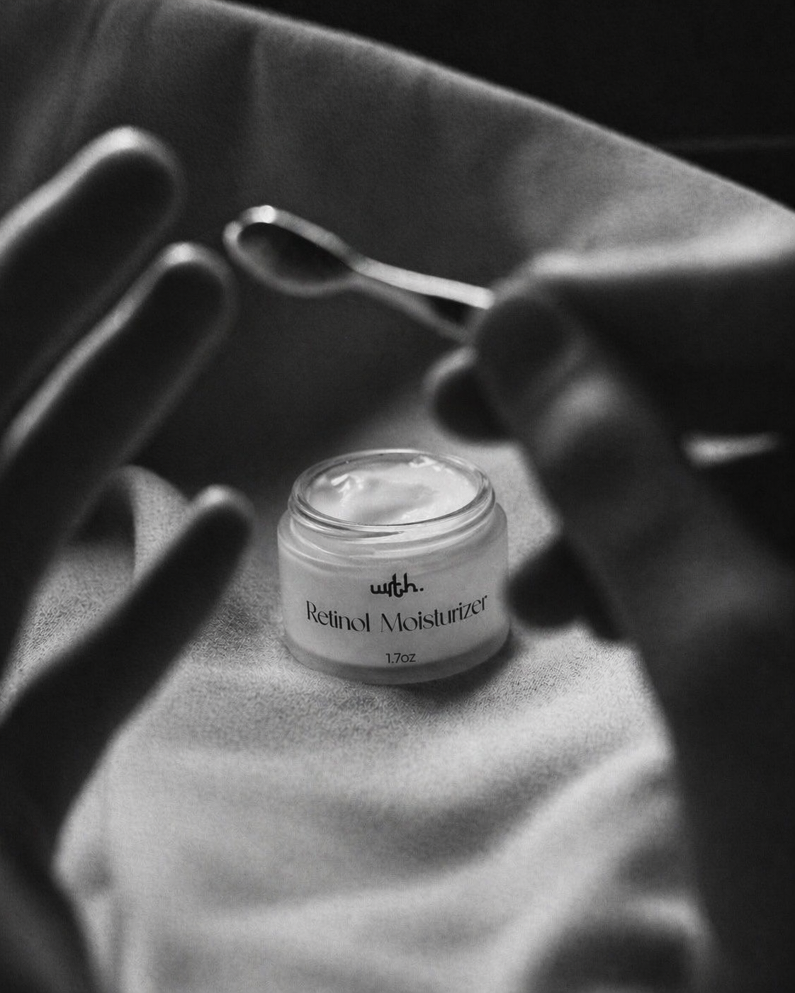 Jar of Retinol Moisturizer with a spoon on a textured surface