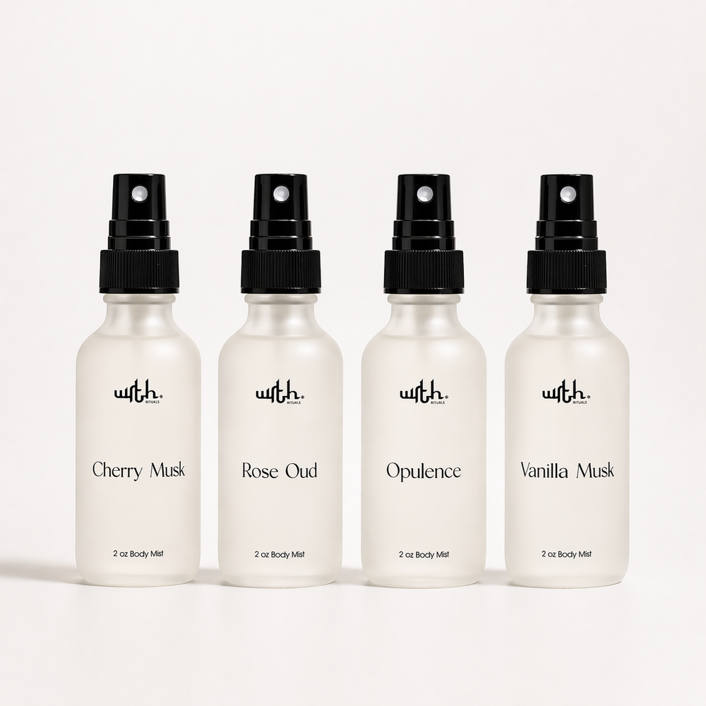 Four white spray bottles with black caps on a white background, labeled with different scents.