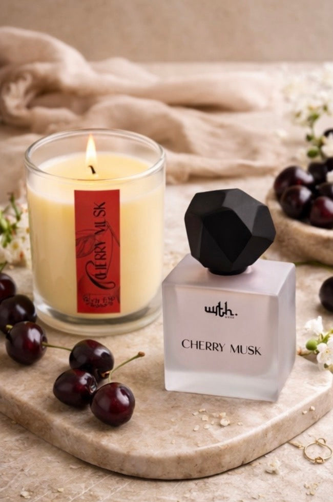 Candle and perfume bottle labeled 'Cherry Musk' on a stone surface with cherries and flowers.