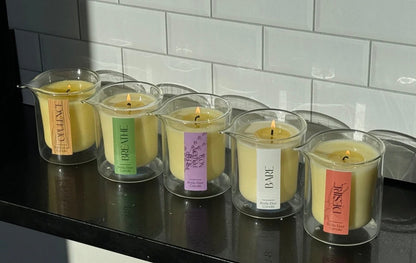 Set of candles in glass containers with labels on a black surface against a tiled wall.