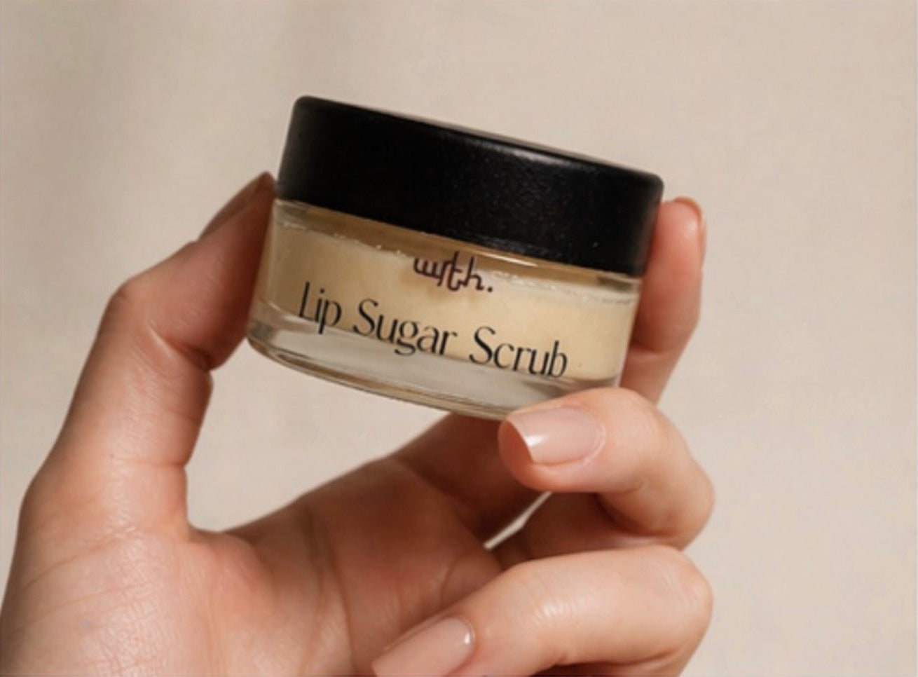 Hand holding a jar of lip sugar scrub with a beige background