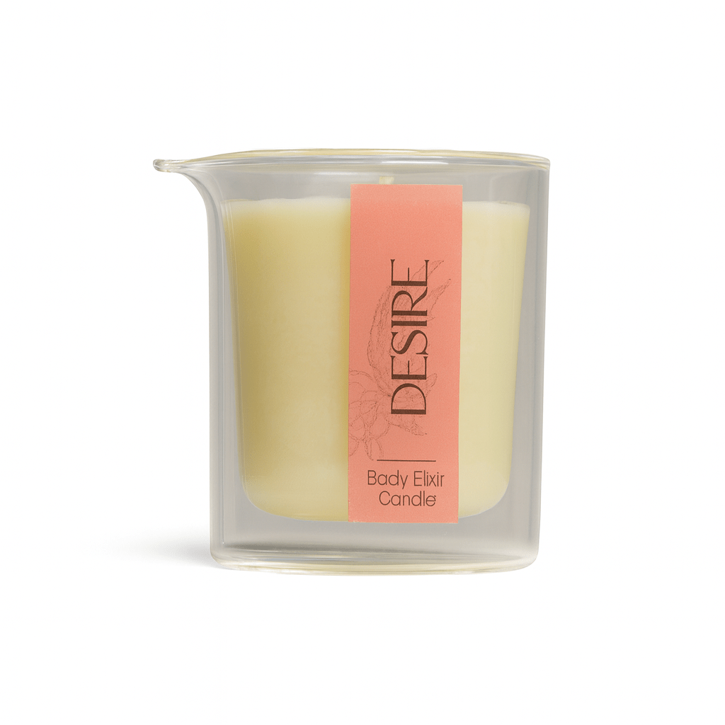 DESIRE Body Elixir Candle in clear glass container with soft yellow wax and coral label
