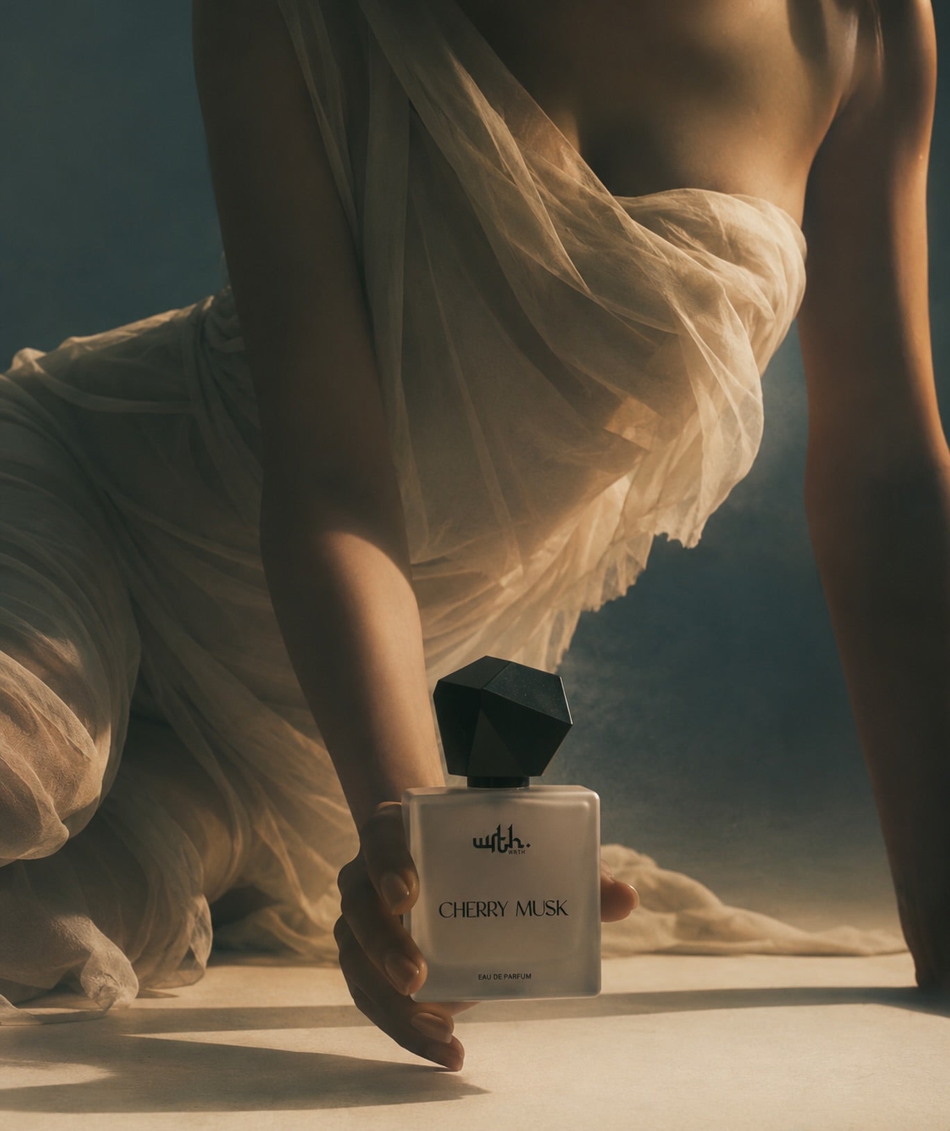 A perfume bottle labeled 'wifls CHERRY MUSA' held by a person draped in flowing cream fabric against a dark blue background.