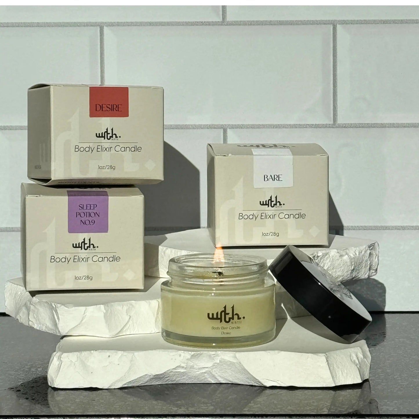 WRTH Studio Body Elixir Candles in Desire, Sleep Potion No.9, and Bare scents with one lit candle in glass jar on white stone slabs