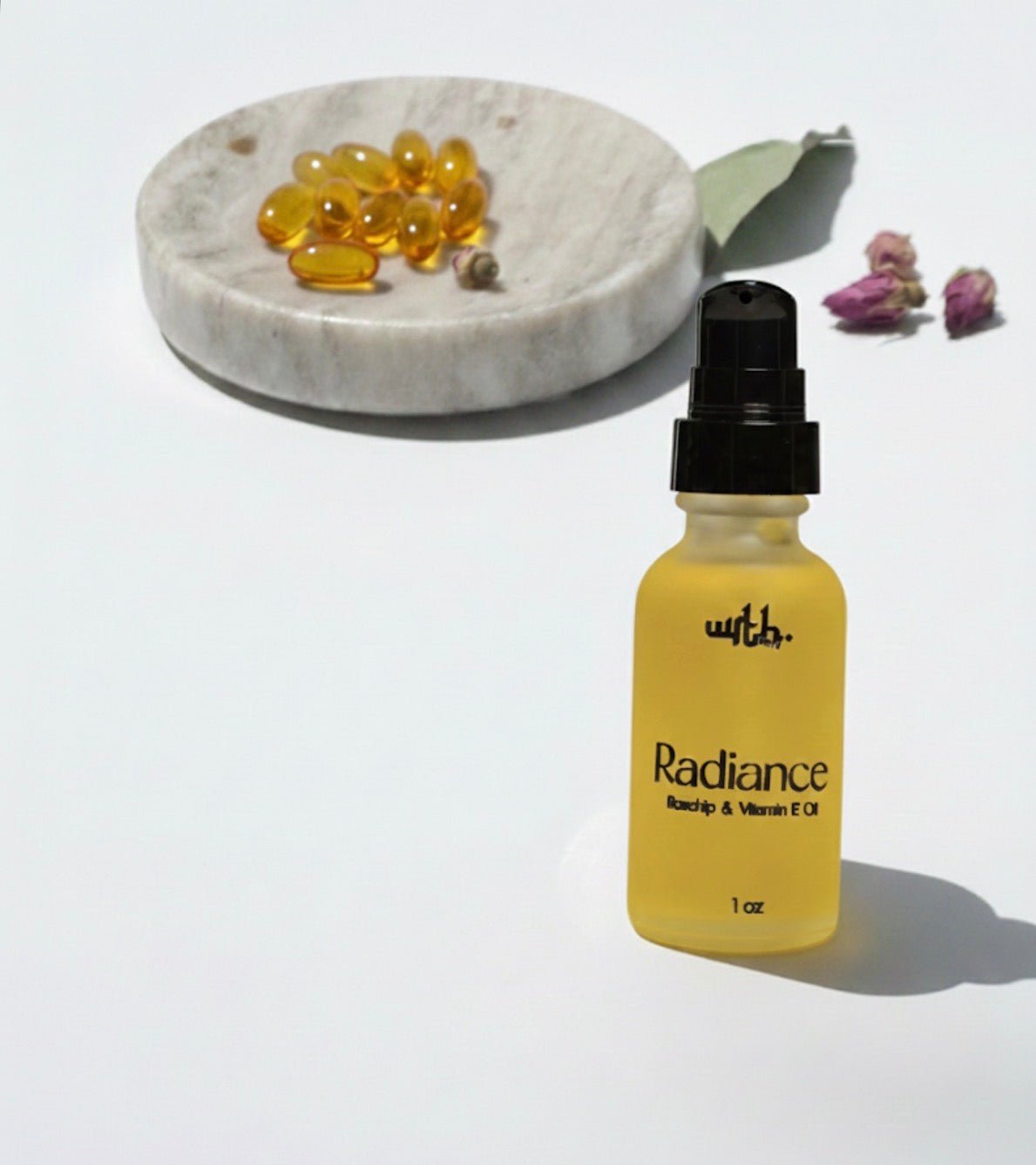 Bottle of WRTH Radiance Rosehip and Vitamin E face oil with capsules on marble dish and dried rose buds